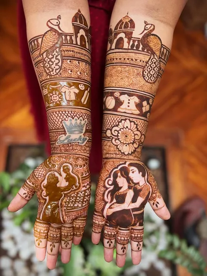 A detailed view of a personalized baby shower mehendi. The design includes couple portraits, traditional palace and peacock motifs, and a band of baby-themed elements like onesies and toys.