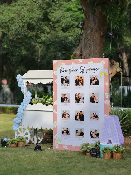 A milestone photo board celebrating "One Year of Arzoie." The board is decorated with a daisy and rainbow motif and placed next to a charming white cart, creating a lovely display corner.