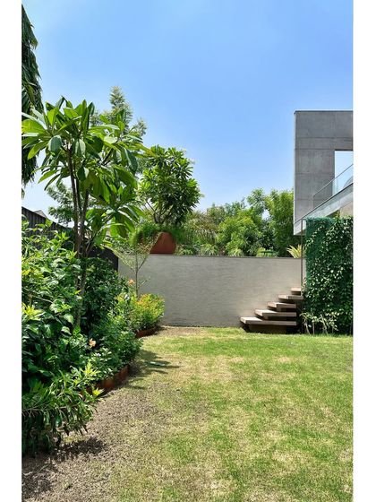 A view of the ground-level garden at the 'House of Terraces'. A simple lawn is enclosed by a textured wall and dense planting, creating a private green space that connects to the terraces above.
