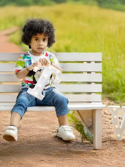 A sweet outdoor portrait of a toddler sitting on a park bench, holding a light-up letter from his "TWO" sign.
