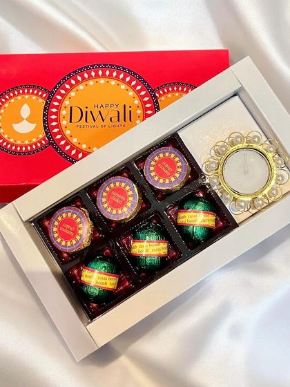A simple yet elegant Diwali gift box containing firecracker-shaped chocolates and a decorative pearl diya, making it a perfect small token of appreciation.