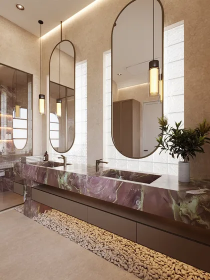 The centerpiece of this spa-like bathroom is the stunning double-sink vanity, crafted from a dramatic pink and green stone. Elongated oval mirrors and pendant lights add a touch of modern elegance.