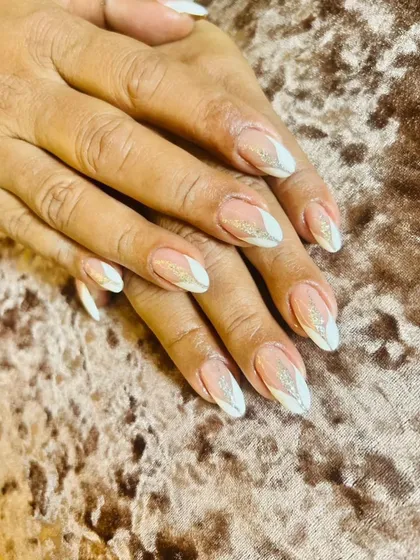 An elegant, pointed almond nail set with a petal-like white tip design and a dusting of fine gold glitter.