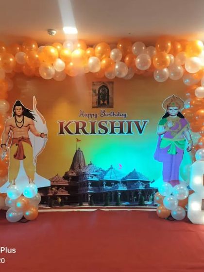 A unique Shree Ram-themed birthday party. This decoration features cutouts of Ram, Sita, and Hanuman against a temple backdrop, framed by an orange and white balloon arch.