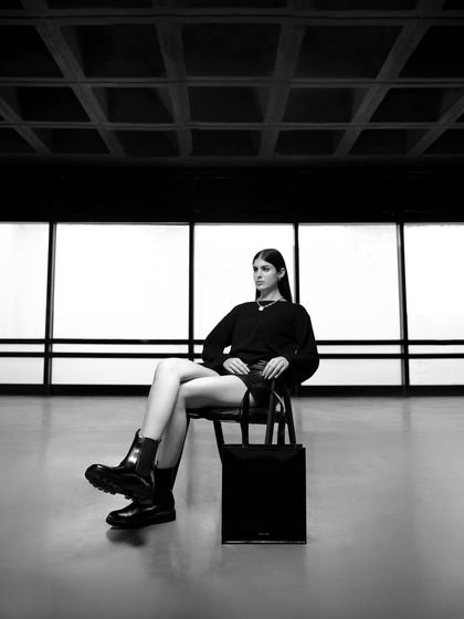 A solo shot of the female model from the Moral Code campaign. The composition is clean and minimalist, highlighting the modern design of the boots and tote bag.