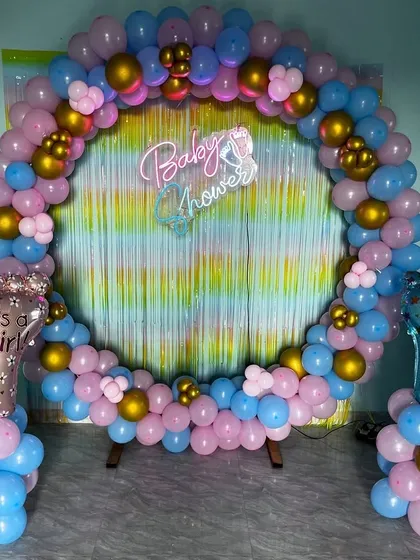 Celebrate the mom-to-be with a beautiful baby shower. This popular gender-reveal setup uses a full balloon ring in pink, blue, and gold, with "It's a Girl" and "It's a Boy" accents, all centered around a shimmering backdrop and a "Baby Shower" neon sign.
