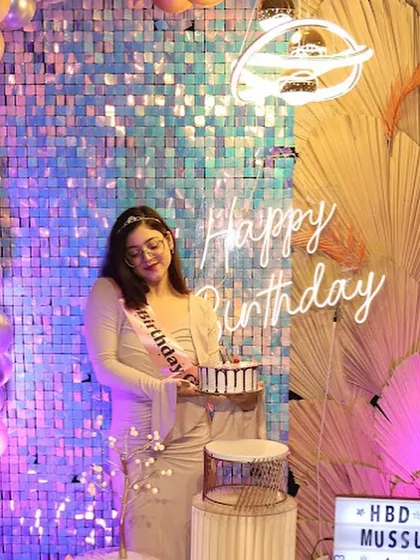 A smiling birthday girl holds her cake in front of a "Happy Birthday" neon sign. Our setups are designed to make the guest of honor feel truly special.