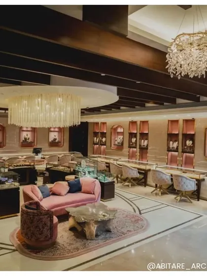 The main floor of Batukbhai Jewellers, showing the amalgamation of different textures and tones. Exposed ceiling beams, multiple chandeliers, and plush, colorful seating come together to create a layered and sophisticated retail environment.