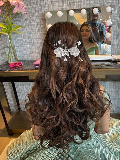 The back of a half updo with soft curls, adorned with a beautiful floral accessory. This look is perfect for a pool party or Mehendi.