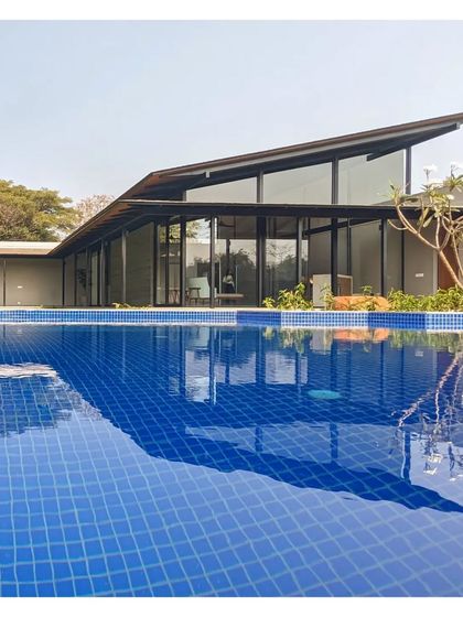 The sharp, angular roof of Villa 15 in Alibaug, reflected in the deep blue pool. The design is a simple, direct solution for a relaxed country life.