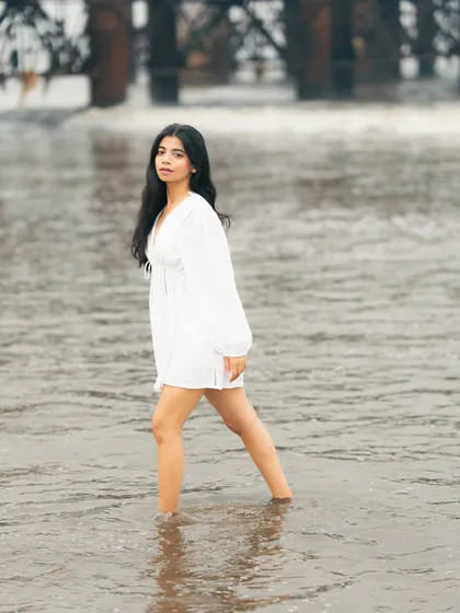 Walking through the water, this shot captures a sense of journey and movement, with the white dress flowing around her.