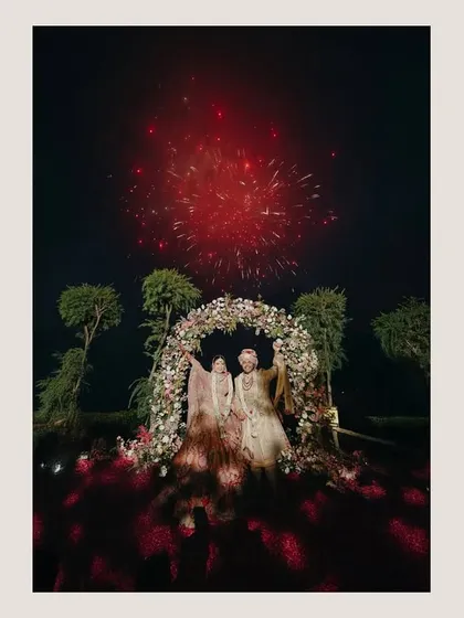 A moment of pure spectacle. This shot captures the couple under a floral arch as fireworks light up the night sky, a grand and unforgettable finale to their wedding celebration.