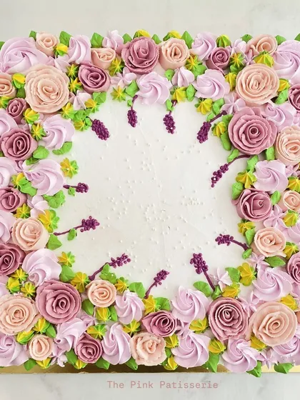 A square cake beautifully framed with a wreath of hand-piped buttercream flowers in pastel shades of pink, purple, and yellow.