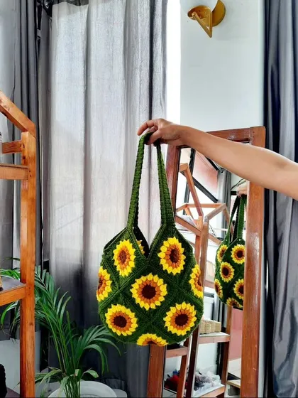 A product shot of my sunflower granny square tote bag. I'm holding it up to show the full pattern, the sturdy construction of the handle, and the deep, rich colors of the green, yellow, and brown yarn I used.