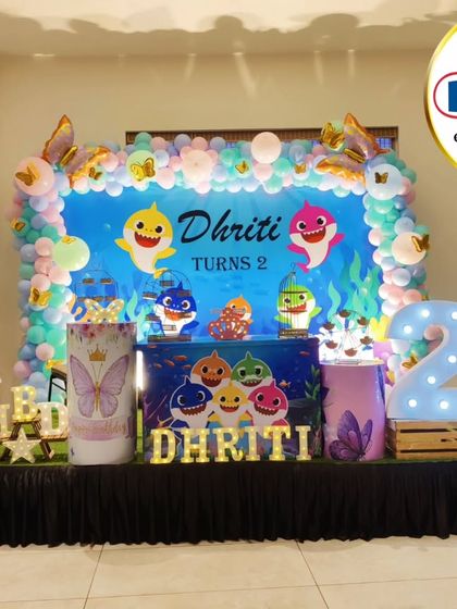 A fun-filled Baby Shark-themed second birthday party. The underwater stage features a large backdrop with the whole shark family, themed plinths, and character cutouts.