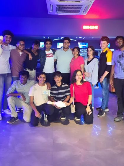A large group of friends posing after a bowling game, with one holding a pin as a trophy.