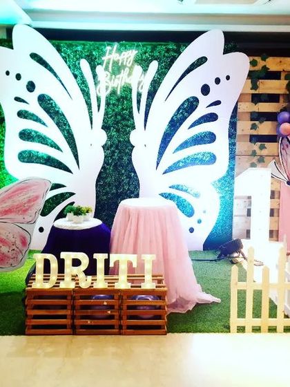 This butterfly-themed decoration for Driti features a similar design with large wing cutouts and a greenery backdrop. The color scheme here uses deep purple and orange balloons, showing how the theme can be adapted to different color preferences.