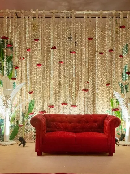 A decadent wedding stage with a red velvet sofa, a backdrop of cascading crystals, and lush white floral arrangements.