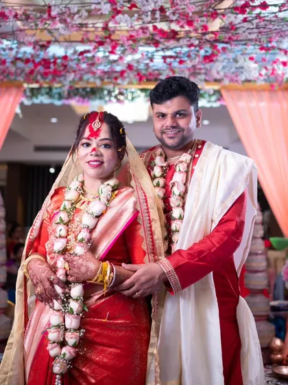 A classic portrait of a newly married Bengali couple under the floral mandap after the completion of their wedding rituals.