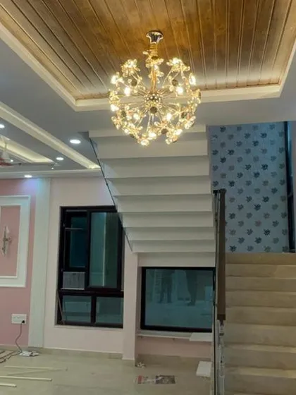 This photo showcases a grand staircase in a duplex home, with a beautiful chandelier hanging from a wood-paneled false ceiling, creating a magnificent focal point.