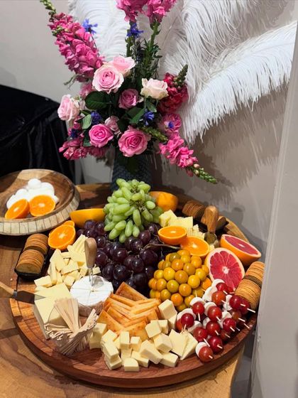Another angle of a spectacular cheese board, showcasing a wheel of Brie, cubed cheeses, and an array of fresh fruits including grapefruit, oranges, and grapes, all arranged on a rustic wooden platter.