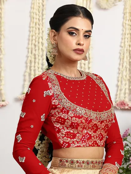 A close-up of the heavily embroidered red blouse, paired with a beige silk lehenga. The butterfly motifs add a whimsical touch.