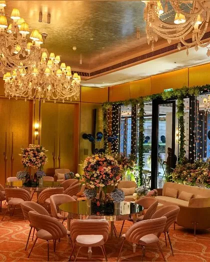 A wider view of the pastel-themed event space, showing the elegant seating arrangements and grand chandeliers inside a sunlit room.