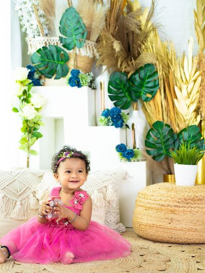 This beautiful princess in a vibrant pink dress is celebrating turning one in a stylish boho and tropical-themed setup.
