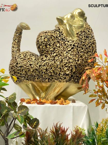 The brass leaf sculpture styled in the gallery, its golden form shining amidst plants, suitable for both indoor and outdoor display.