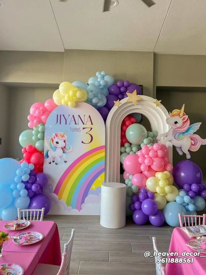 A colorful rainbow unicorn theme for a third birthday. This decor features a double-arched backdrop, a cascade of rainbow-colored balloons, and cute unicorn cutouts.