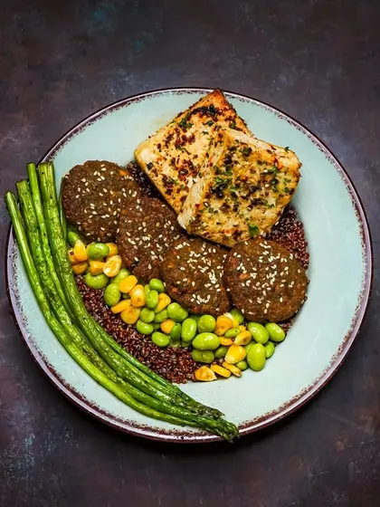 A falafel and quinoa bowl with edamame, asparagus, and grilled halloumi or paneer. The dark, textured backdrop and careful styling elevate this healthy dish into a gourmet experience.