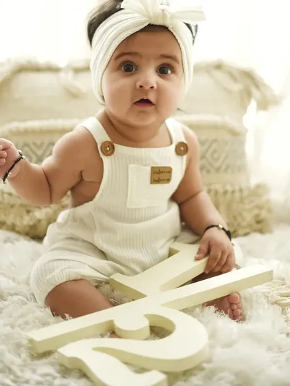 A slightly different angle from the six-month session, capturing a curious and sweet expression. The simple white outfit and background keep the portrait feeling fresh and timeless.