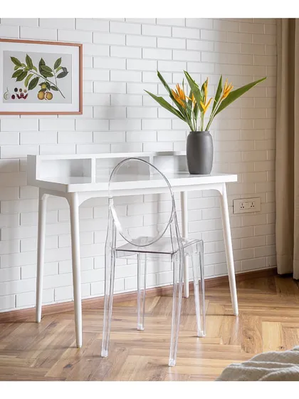 The study in 'Vishu Home' is a minimalist's dream. A clean white desk and a transparent ghost chair create a sense of lightness and space, set against a white brick-textured wall for a touch of industrial chic.