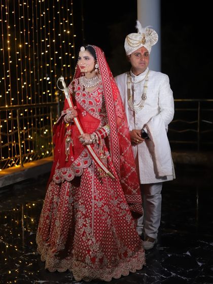 The perfect couple shot. The bride in her red lehenga and the groom in his white sherwani make a beautiful pair. Her makeup is classic and elegant, perfect for wedding photos.