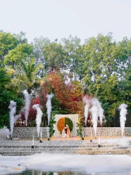 A wide shot of the varmala ceremony, showing the scale of the celebration with smoke effects rising from the 'kund'.