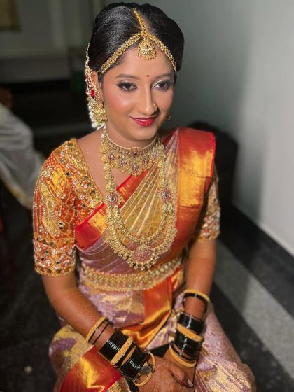 My bride Monika, looking radiant for her Muhurtham. We chose a classic look with a red-orange Kanjivaram saree, complemented by gold jewelry and a bright red lip.