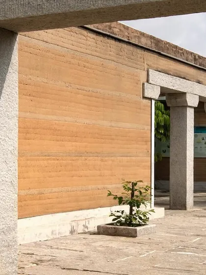 The interplay of rammed earth walls and granite stone pillars at the H.N. Science Center. This combination of two fundamental materials, earth and stone, forms the core of the building's identity.