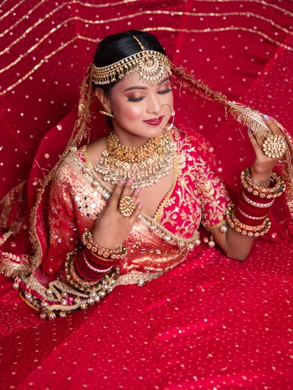 A stunning overhead shot of the bride, with her red lehenga spread out. The makeup is flawless, with a focus on the eyes and traditional jewelry.