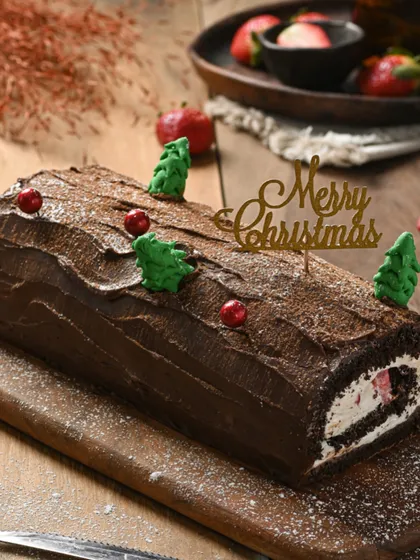 A festive chocolate Yule log, decorated with mini Christmas trees and a "Merry Christmas" topper. A delicious and traditional holiday dessert.