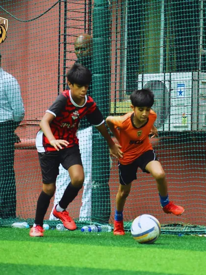 A young player dribbling with speed and agility, with parents watching in the background.