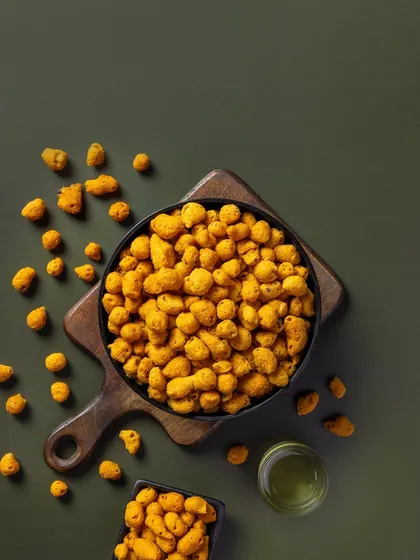 Coated peanuts against a muted green background. This composition is designed for packaging, with negative space for branding and text.