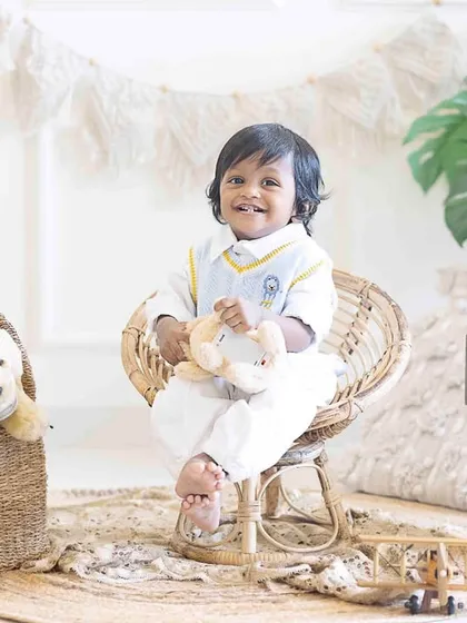 A big smile for his first birthday. Seated in a small wicker chair, this little boy's happiness is the centerpiece of the photograph.