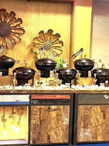 A rustic and industrial-style buffet setup for a Diwali event. The black serving dishes contrast beautifully with the warm wood and illuminated base of the counters.