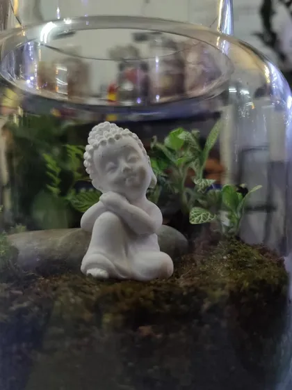 Personalize your terrarium to create a peaceful scene. This close-up shows a finished piece from one of our workshops, featuring a serene Buddha miniature nestled amongst fittonia plants and soft moss.