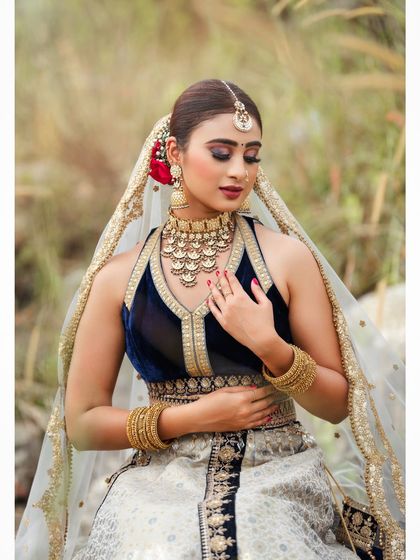 An outdoor bridal shoot capturing a serene and elegant moment. The natural setting complements the traditional lehenga, and the soft lighting highlights the delicate details of the fabric and embroidery.