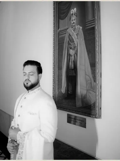 A contemplative black and white portrait of the groom standing next to a royal portrait, creating a powerful juxtaposition of past and present.