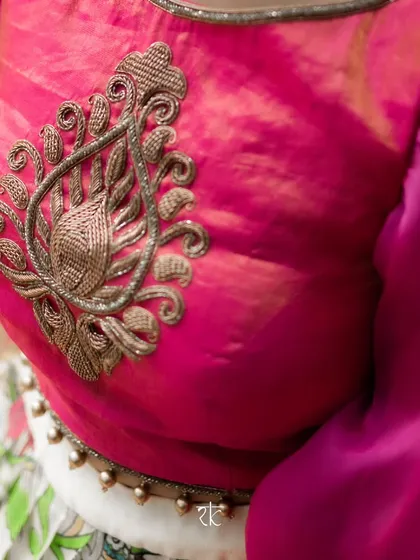 A close-up of the intricate zardosi motif on the chest of a vibrant pink blouse. The craftsmanship adds a touch of royal elegance to the contemporary design with its full bishop sleeves.