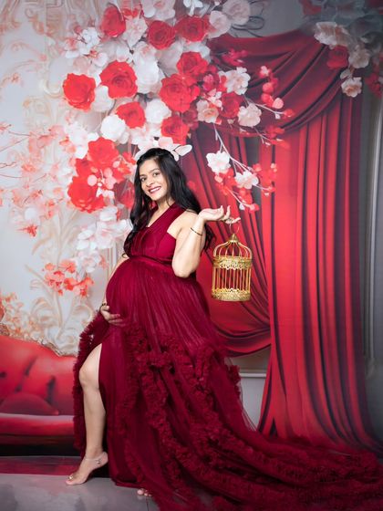 A joyful solo maternity shot of a mother-to-be in a flowing red gown, holding a decorative golden birdcage.