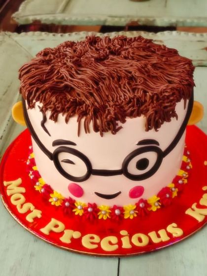 A quirky and cute cake designed to look like a winking face with glasses and textured buttercream hair.