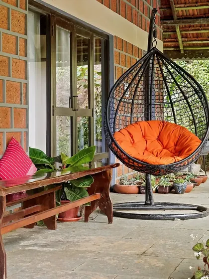 A cozy outdoor seating area at Magnolia Resorts, Coorg, featuring a comfortable swing chair with a bright orange cushion. This is the perfect spot to relax and enjoy the surrounding nature.